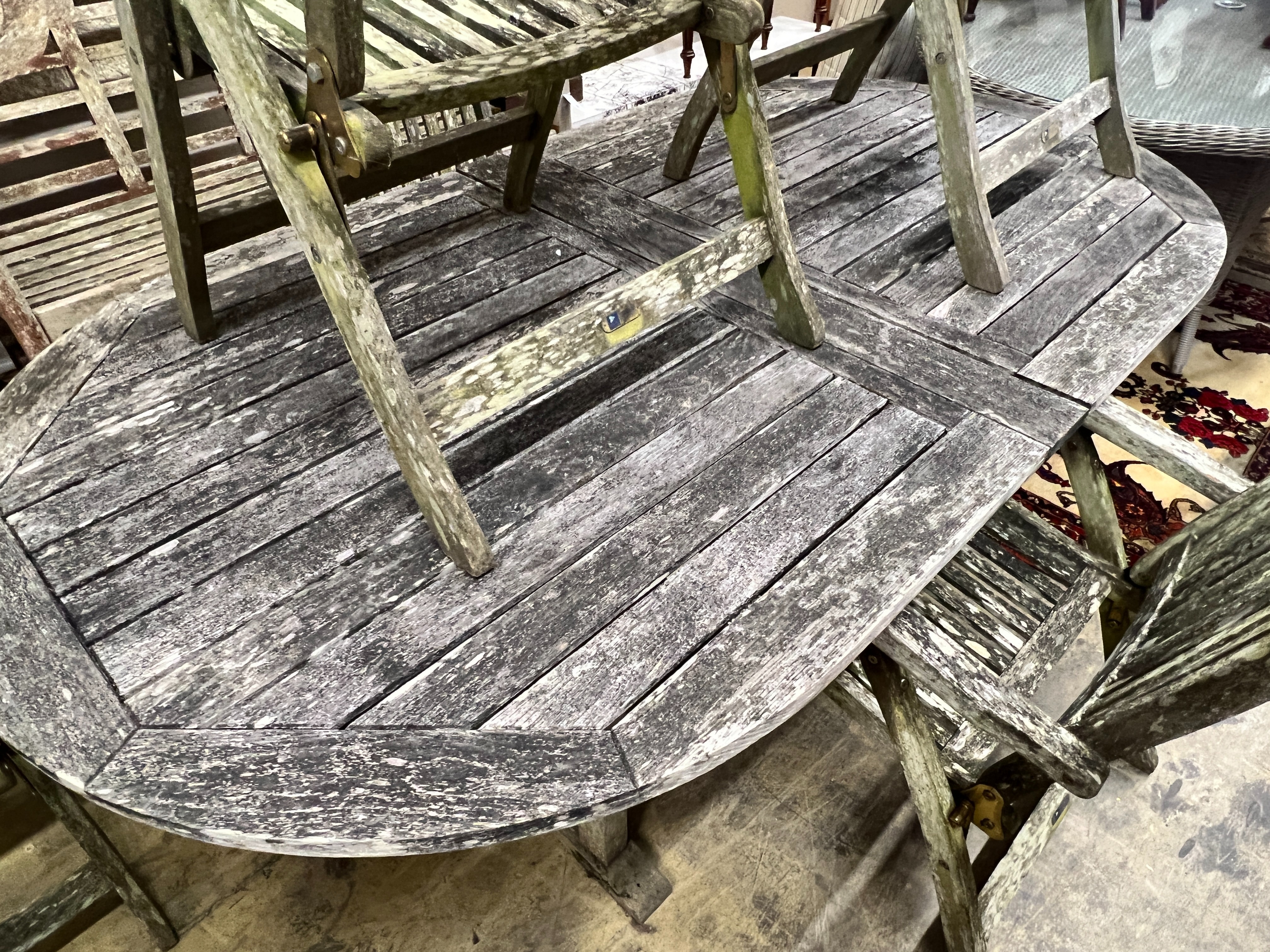 A weathered teak oval extending garden table, extended 250cm, width 109cm, height 73cm, together with six weathered teak folding garden elbow chairs